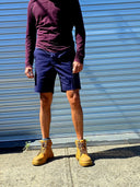 Person wearing a long-sleeve maroon shirt, navy shorts, and brown work boots standing in front of a blue metal shutter.