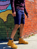 Person wearing navy shorts and brown boots standing in front of a colourful brick wall.