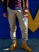 Person wearing khaki pants and yellow boots holding a white cylindrical object against a blue and yellow background.